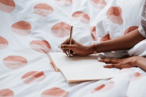 A woman journaling on a bed with polka dot sheets, creating a cozy atmosphere.
